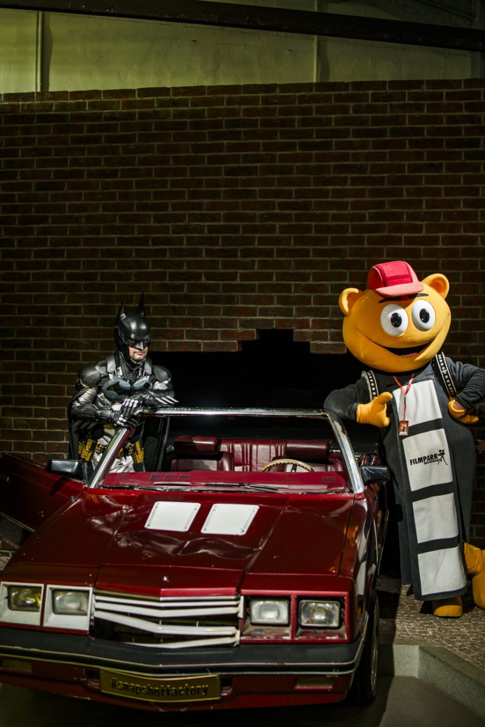 Batman und das Maskottchen Flimmy posieren in einem Auto