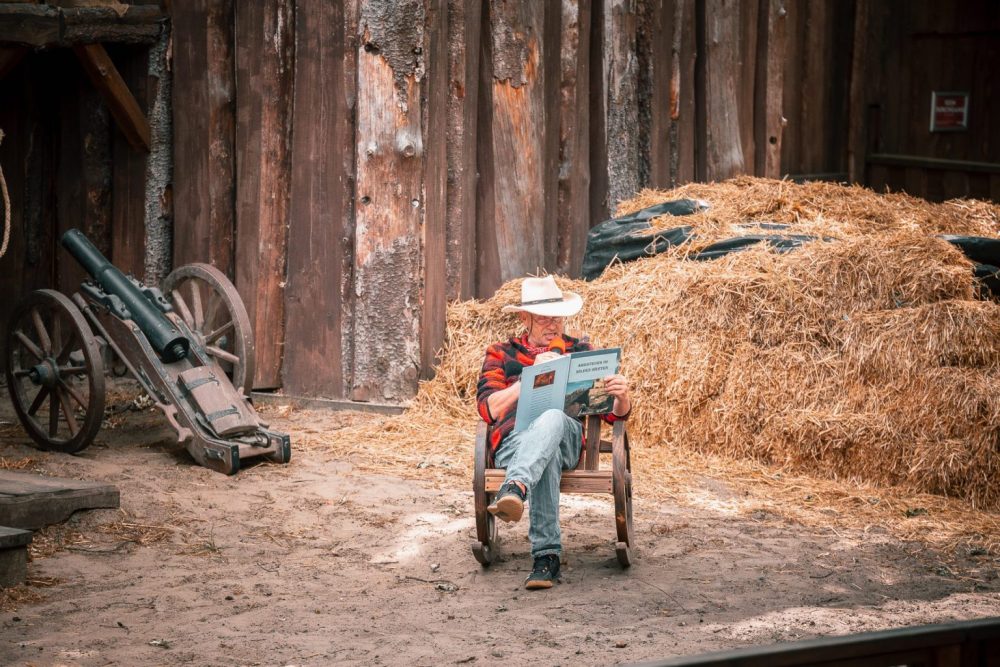 Mann mit Cowboyhut auf Schaukelstuhl liest vor