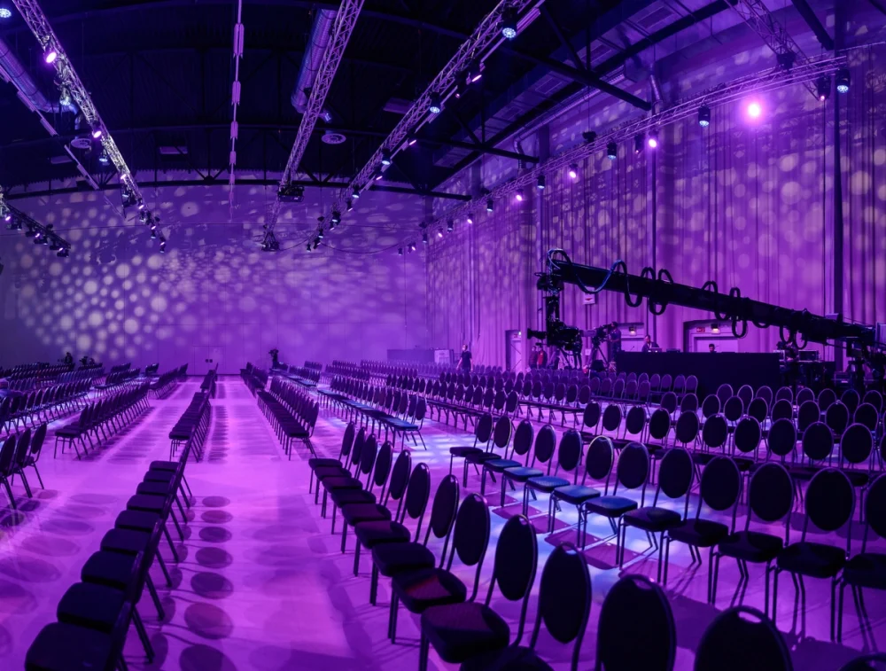 Voll bestuhlter Saal in pink-lila Beleuchtung